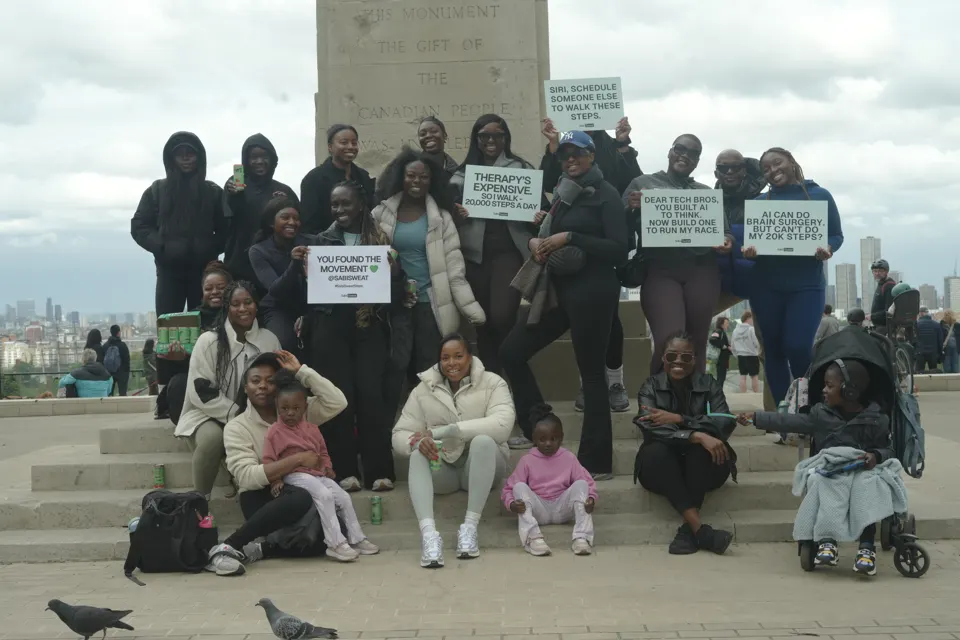The Sabi Sweat community on monument steps with their walking signs, London skyline behind