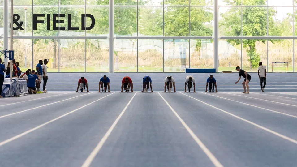 Members crouched at the start line of an indoor athletics track, ready to race